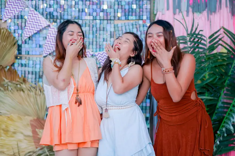 Three teammates laughing in front of a sequined photo wall